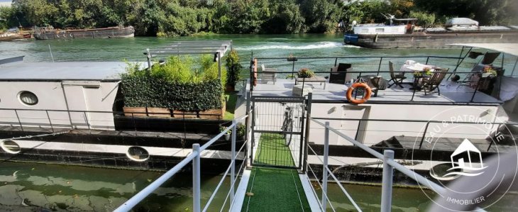 Bateau-logement de type houseboat construit sur une ancienne barge avec une grande surface habitable.